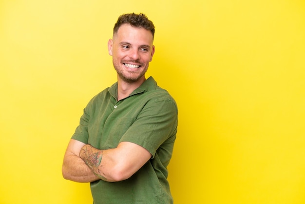 Young caucasian handsome man isolated on yellow background with arms crossed and happy