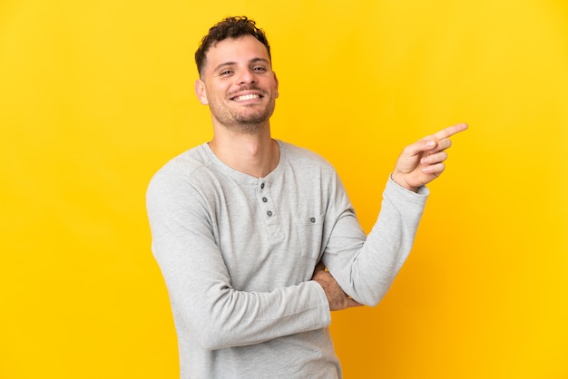 Young caucasian handsome man isolated on yellow pointing finger to the side