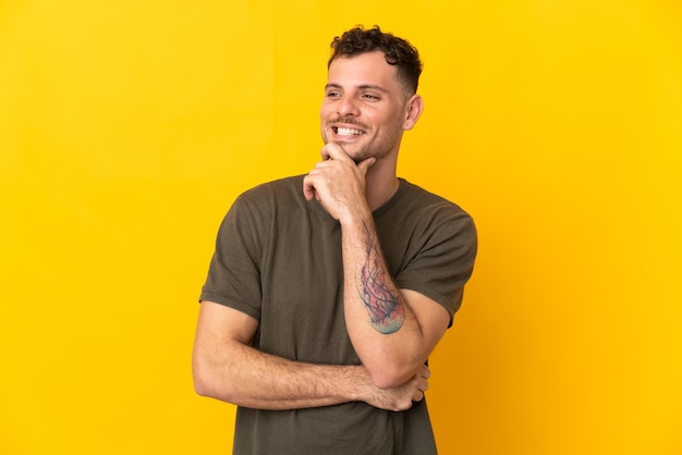 Young caucasian handsome man isolated on yellow wall looking to the side and smiling