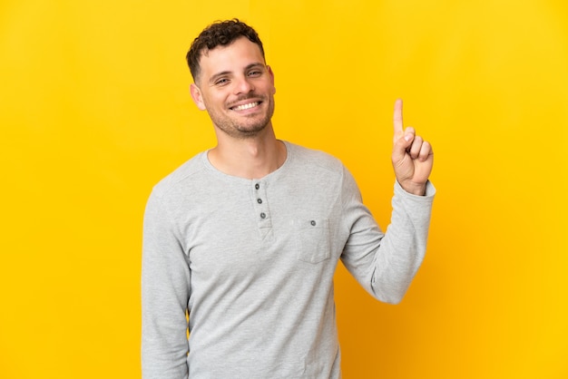 Young caucasian handsome man isolated on yellow wall showing and lifting a finger in sign of the best