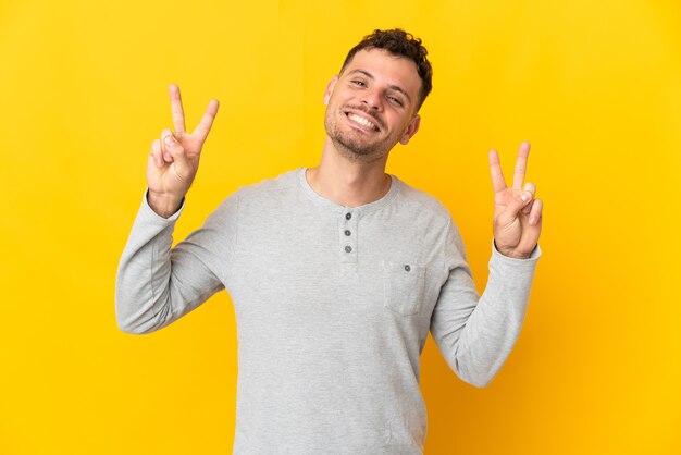 Young caucasian handsome man isolated on yellow wall showing victory sign with both hands