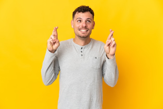 Young caucasian handsome man isolated on yellow wall with fingers crossing and wishing the best