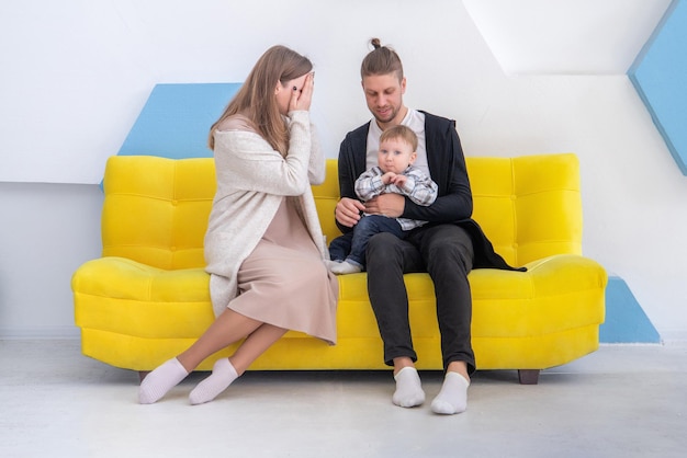 Young caucasian happy family with his little kid having fun on sofa in bright interior