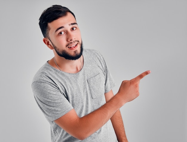 Young caucasian hipster man wearing gray shirt over isolated background cheerful with a smile of face pointing with hand and finger up to the side with happy and natural expression on face