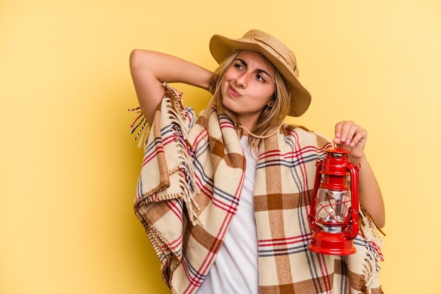 Young caucasian holding lantern isolated on yellow background  touching back of head, thinking and making a choice.