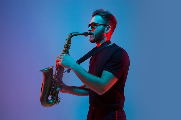 Young caucasian jazz musician playing the saxophone on gradient bluepurple studio