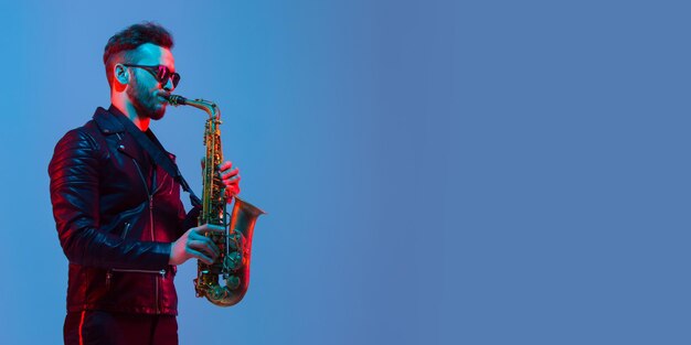 Young caucasian jazz musician playing the saxophone in neon light, flyer