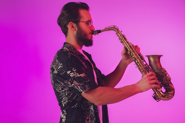 Young caucasian jazz musician playing the saxophone in neon light