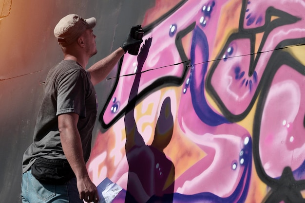 Young caucasian male graffiti artist drawing big street art painting in blue and pink tones