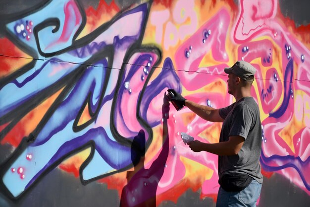 Young caucasian male graffiti artist drawing big street art painting in blue and pink tones