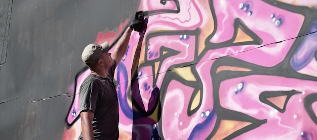 Young caucasian male graffiti artist drawing big street art painting in blue and pink tones