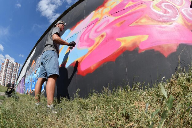 Young caucasian male graffiti artist drawing big street art painting in blue and pink tones