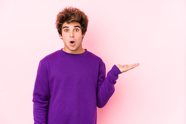 Young caucasian man against a pink  isolated impressed holding copy space on palm.