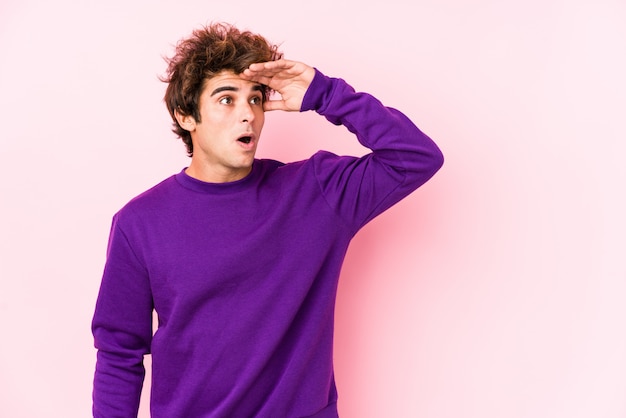 Young caucasian man against a pink wall isolated looking far away keeping hand on forehead.