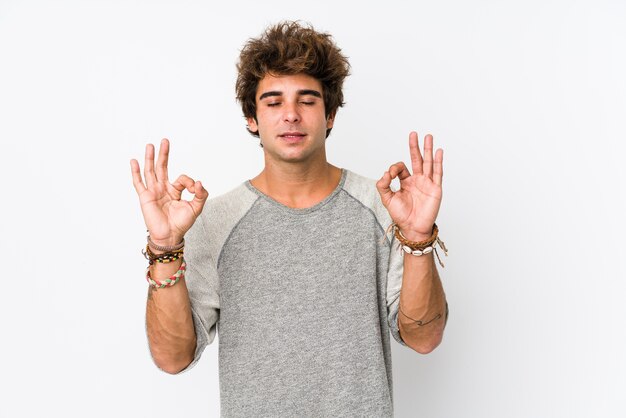 Young caucasian man against a white wall isolated relaxes after hard working day, she is performing yoga.