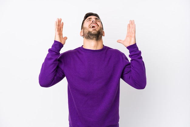 Young caucasian man against a white wall isolated screaming to the sky, looking up, frustrated.