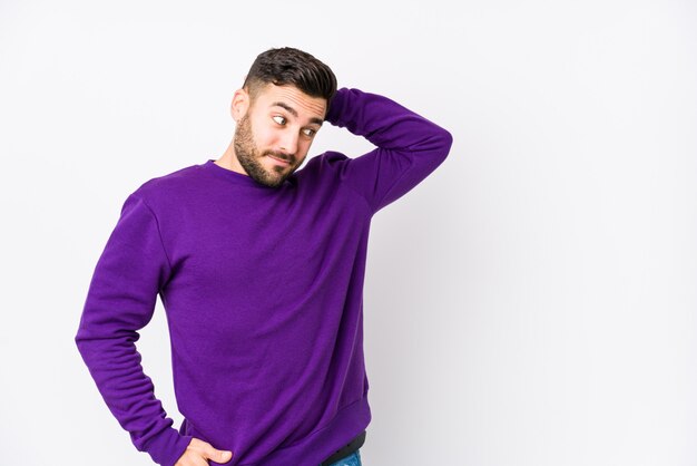 Young caucasian man against a white wall isolated touching back of head, thinking and making a choice.