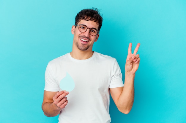 Young caucasian man celebrating world water day isolated joyful and carefree showing a peace symbol with fingers.