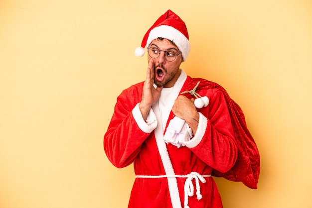 Photo young caucasian man disguised as santa isolated on yellow background is saying a secret hot braking news and looking aside