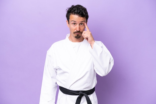 Young caucasian man doing karate isolated on purple background thinking an idea