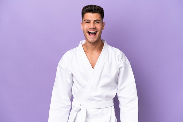 Young caucasian man doing karate isolated on purple background with surprise facial expression