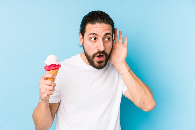 Young caucasian man eating an ice cream isolated trying to listening a gossip.