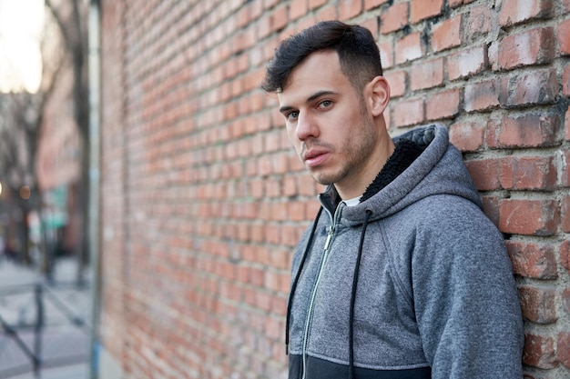 Young caucasian man exudes coolness leaning against a brick wall in the street