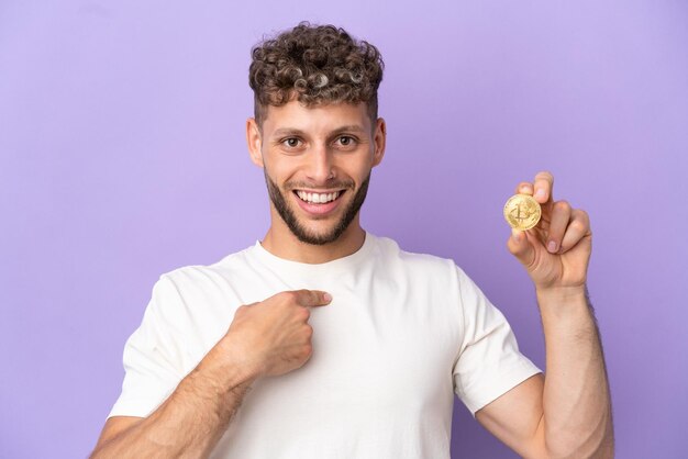 Young caucasian man holding a Bitcoin isolated on purple background with surprise facial expression