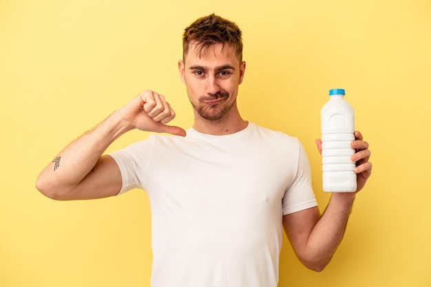 Young caucasian man holding a bottle of mil isolated on yellow background feels proud and self confident, example to follow.