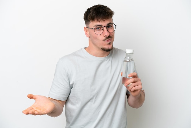 Young caucasian man holding a bottle of water isolated on white background making doubts gesture while lifting the shoulders