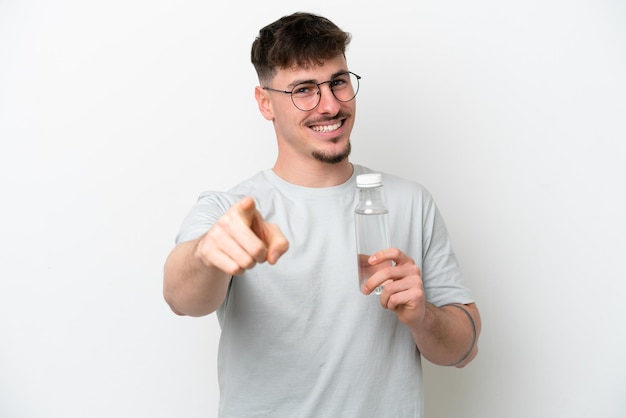 Young caucasian man holding a bottle of water isolated on white background points finger at you with a confident expression