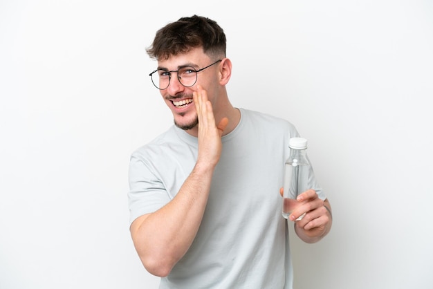 Young caucasian man holding a bottle of water isolated on white background whispering something