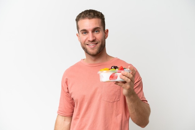 Young caucasian man holding a bowl of fruit isolated on white background smiling a lot