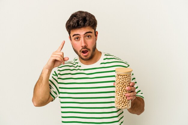 Young caucasian man holding chickpeas jar isolated on white background having an idea, inspiration concept.