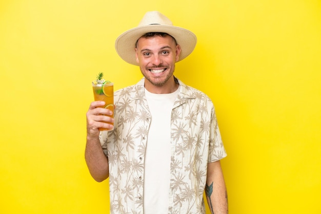 Young caucasian man holding a cocktail isolated on yellow background with surprise facial expression