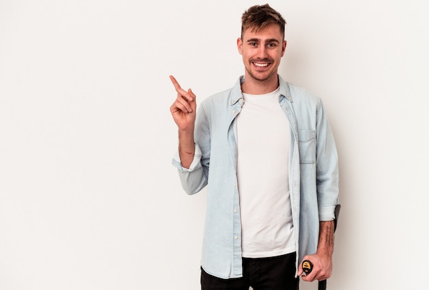 Young caucasian man holding crutch isolated on white background smiling and pointing aside, showing something at blank space.