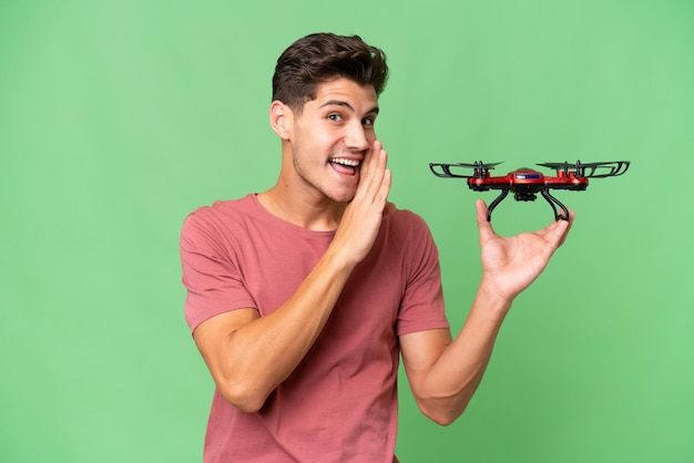 Young caucasian man holding a drone over isolated background whispering something