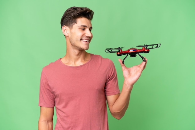 Young caucasian man holding a drone over isolated background with happy expression