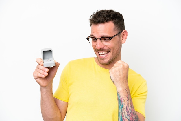 Young caucasian man holding a engagement ring isolated on white background celebrating a victory