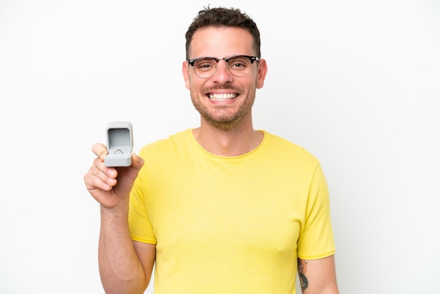 Young caucasian man holding a engagement ring isolated on white background smiling a lot