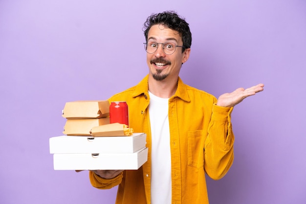 Young caucasian man holding fast food isolated on purple background with shocked facial expression