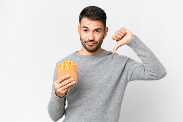 Young caucasian man holding fried chips over isolated white background showing thumb down with negative expression