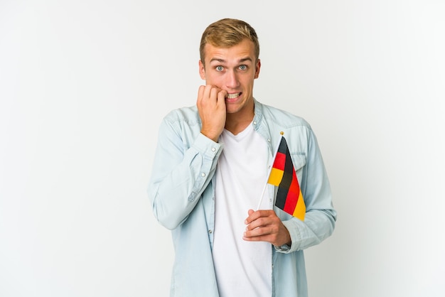 Young caucasian man holding a german flag isolated on white background confused, feels doubtful and unsure.