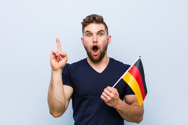 Photo young caucasian man holding a germany flag having some great idea, concept of creativity.