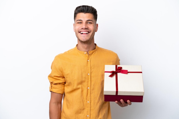 Young caucasian man holding a gift isolated on white background smiling a lot