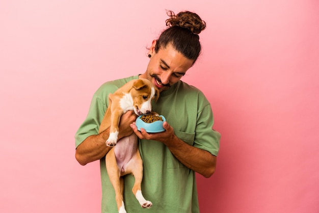 Photo young caucasian man holding his puppy and his food isolated on pink background