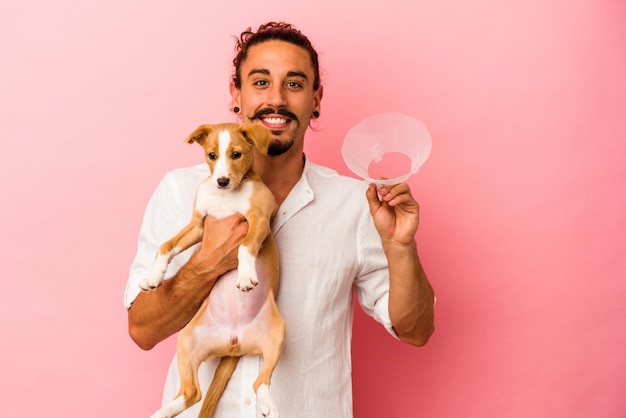 Young caucasian man holding his puppy and protection collar isolated on pink background