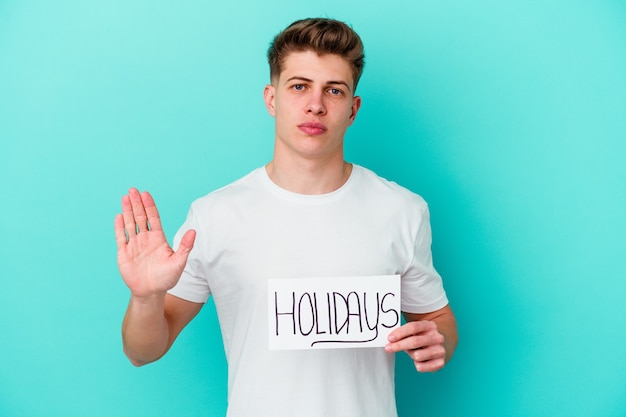 Young caucasian man holding a Holidays placard isolated on blue wall