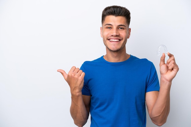 Young caucasian man holding invisible braces isolated on white background pointing to the side to present a product