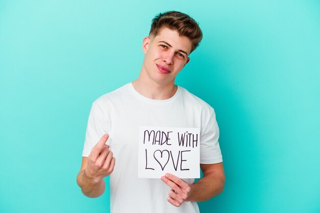 Young caucasian man holding a made with love placard isolated on blue wall